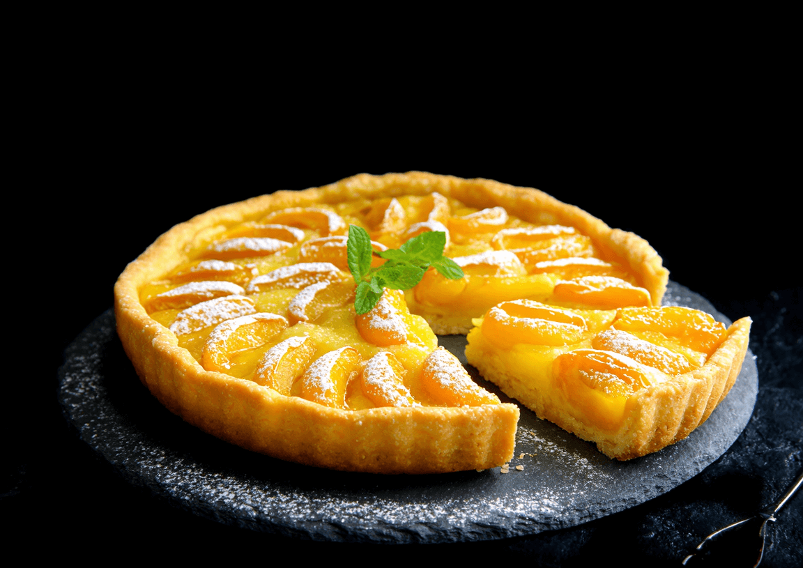 Photo d’une tartelette aux mirabelles dorée sur une ardoise, décorée d’un peu de sucre glace et d’herbes fraîches